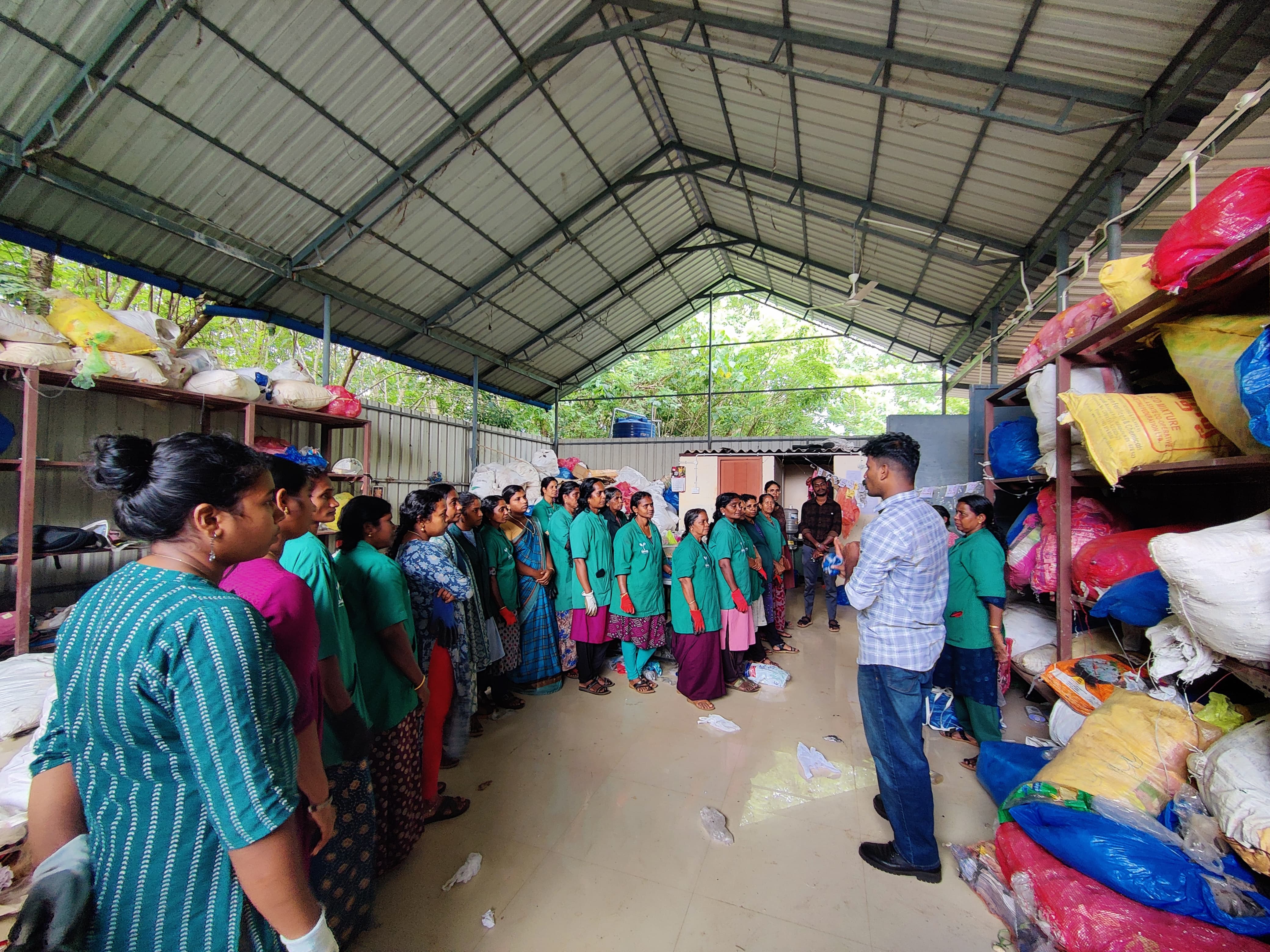 Textile recovery facility with workers in green uniforms sorting and organizing textile materials under warehouse structure